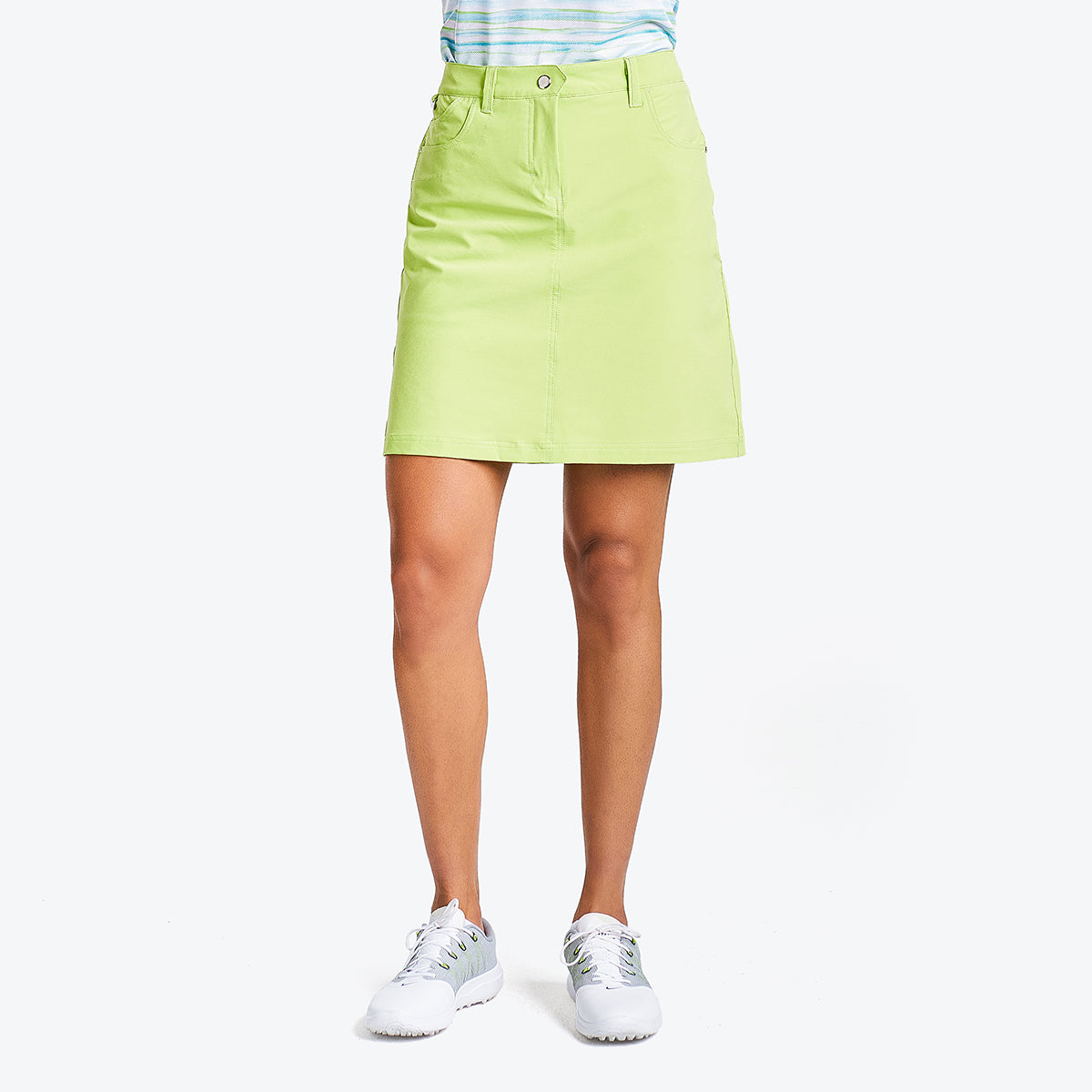 A woman wearing a green skort with pockets and a YKK zipper, paired with a blue and white striped top and white shoes.
