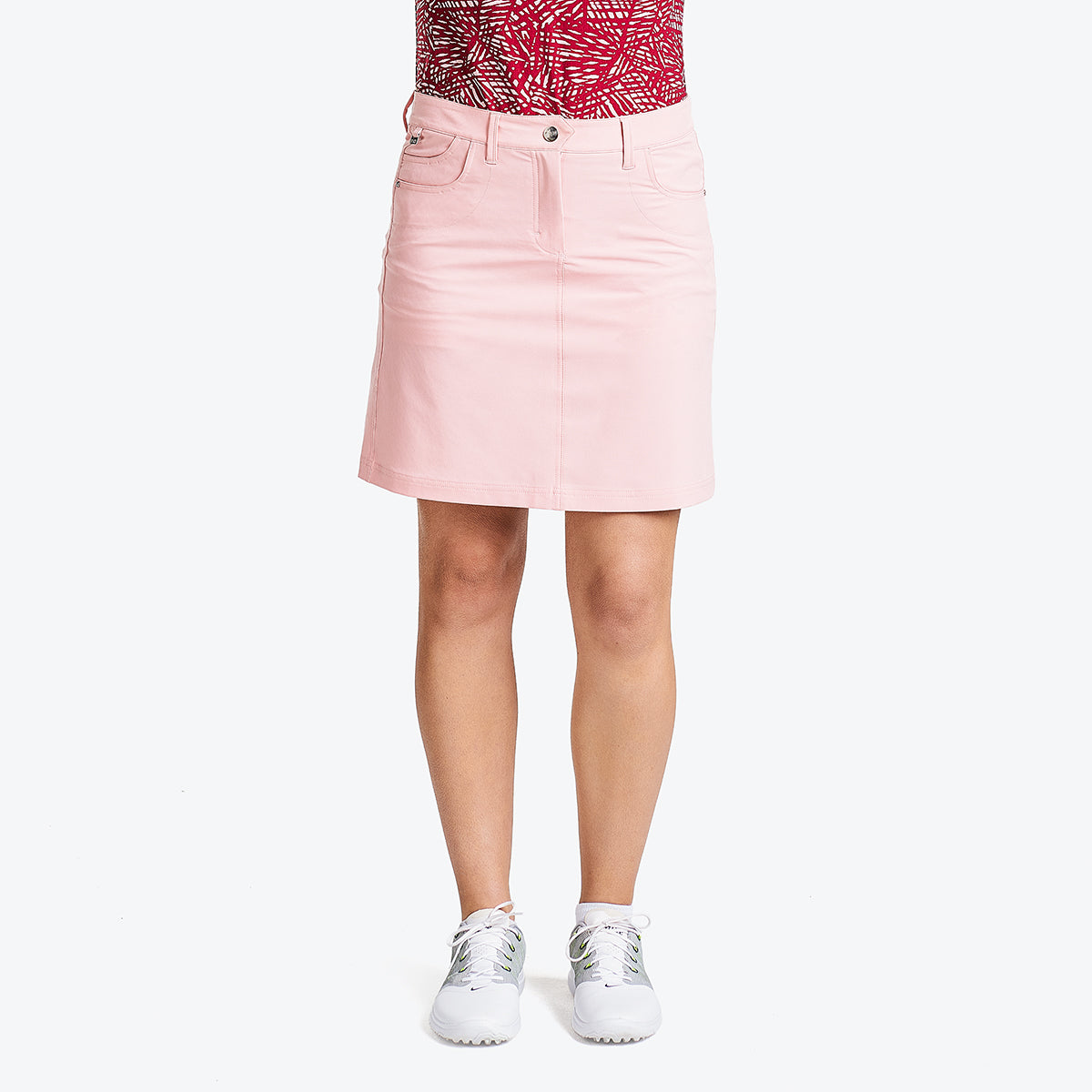 A woman wearing a pink skort and white sneakers, standing against a white background.