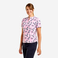 A woman modeling a short-sleeve polo shirt with a pink background and a dark gray feather pattern, paired with navy pants, against a light gray studio background.